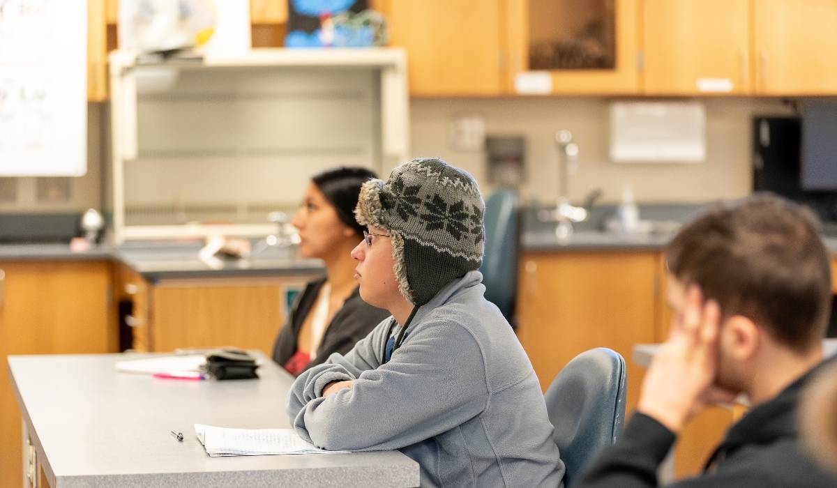 Student in classroom listening to lecture with notebook on table