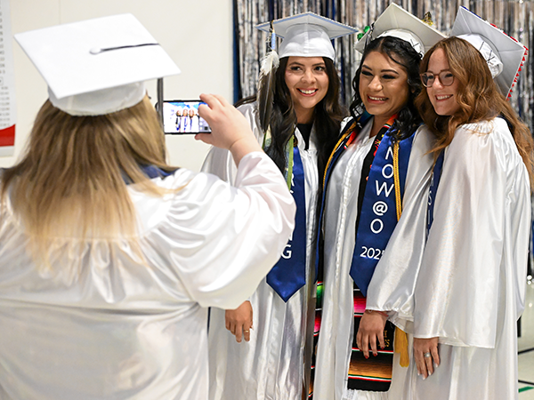 Three WVC Omak graduates smile for a photo, while another graduate takes the photo.