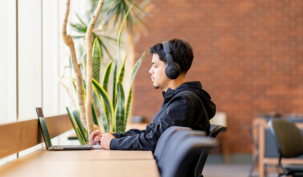 A student sits at a long table and works on a laptop.