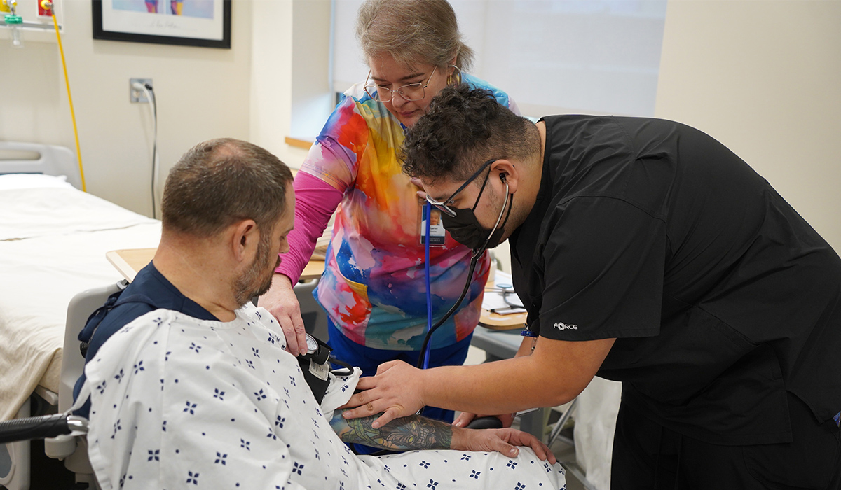 A certified nursing assistant student checks the blood pressure on a patient sitting in a wheelchair.
