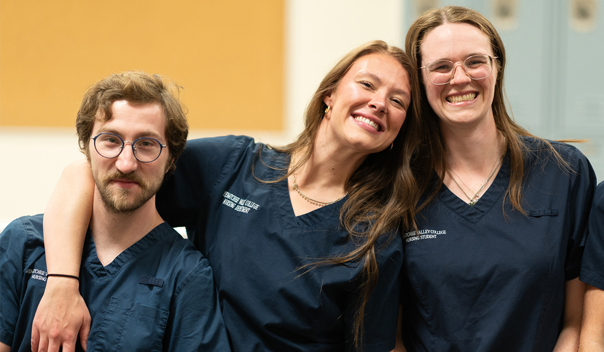 Three nursing students in blue scrubs smile at the camera.