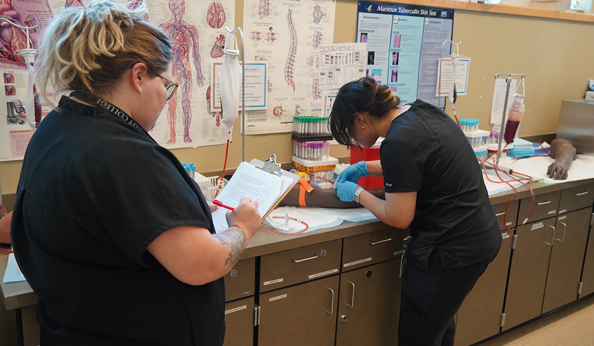 A student places a needle in a manikin arm.