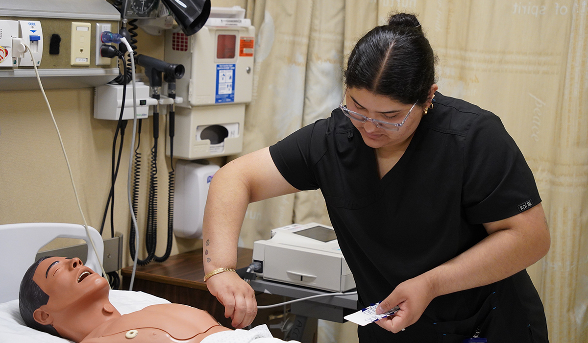 A medical assistant student places devices on a manikin.