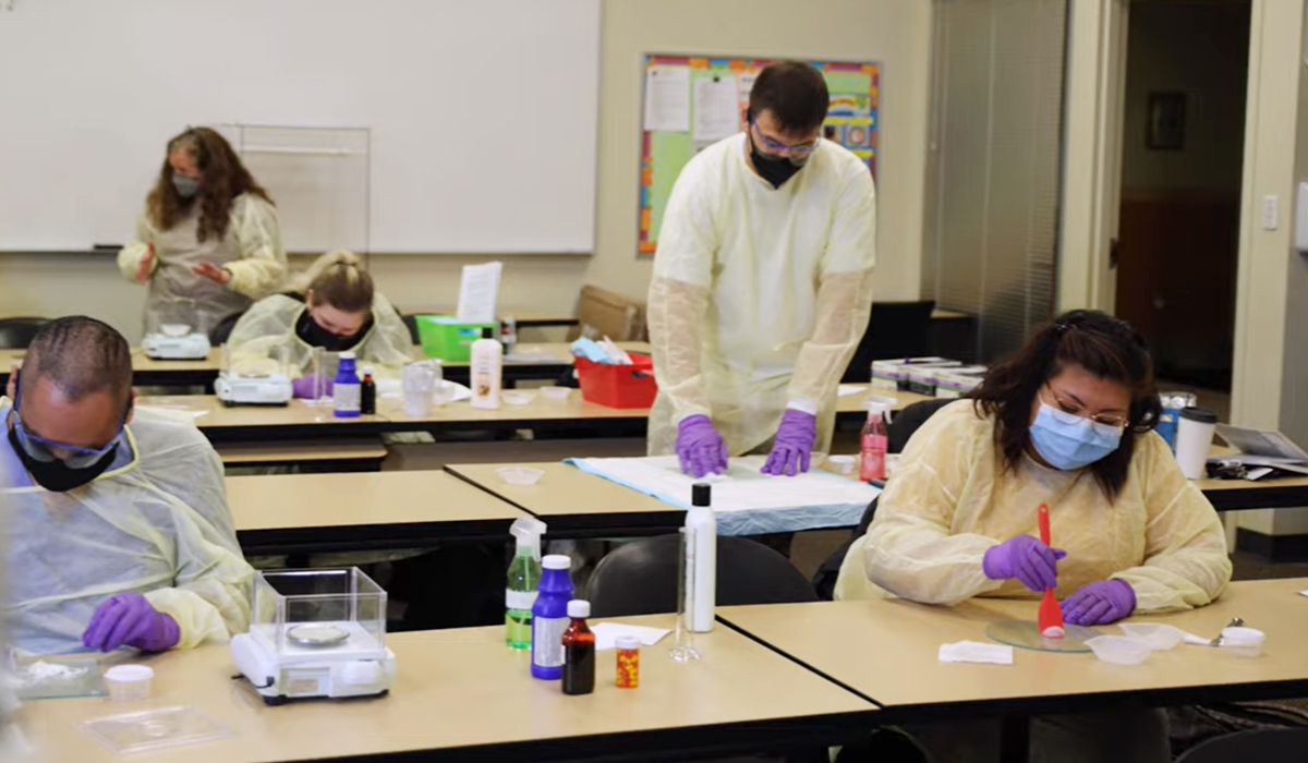 Pharmacy tech students sit at long tables in a classroom and work on dispensing medicine.