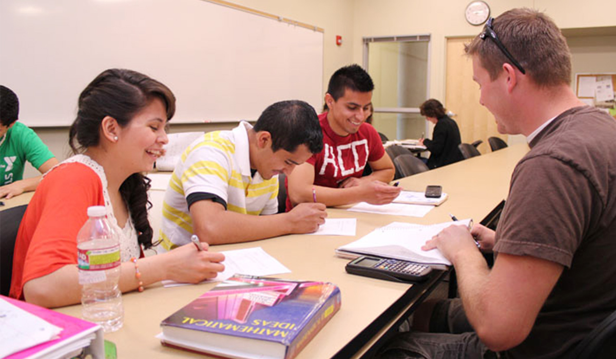 A group of math students with calculators, textbooks, and notes sit in a group at a table.