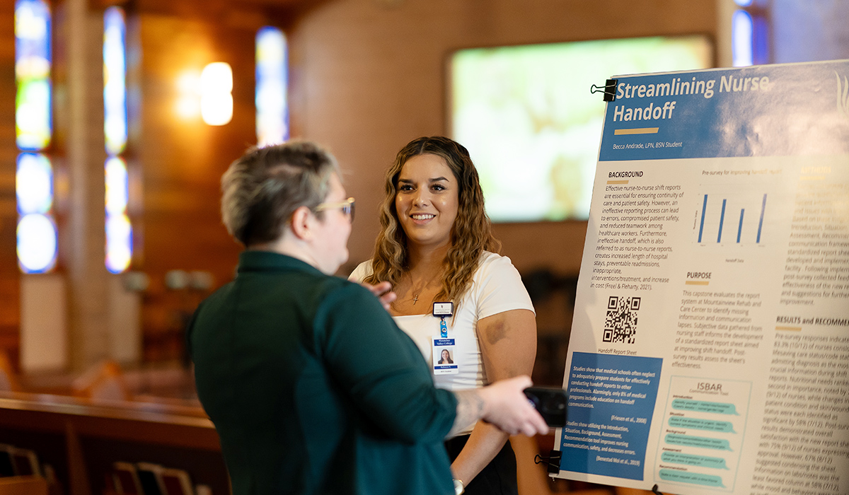 An LPN graduate stands next to her poster presentation at the LPN convocation.