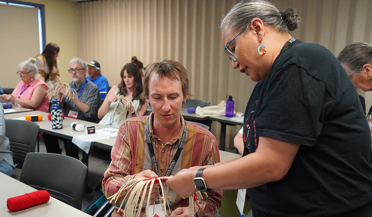 A Native instructor helps a man with a basket-weaving project.