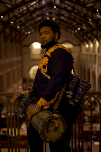 Javoen Byrd standing on a balcony with drums strapped to his shoulder and waist